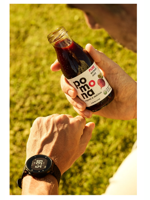 Person holding a bottle of Beet Juice, Organic, Cold-Pressed, 8.4oz, by Pomona with grass in the background