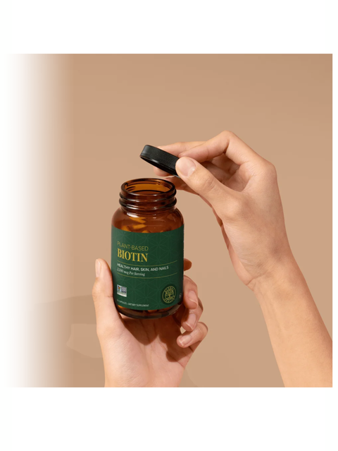 Hand holding a bottle labeled 'Biotin' against a beige background