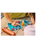 A lifestyle shot of a person playing a colorful board game on a wooden deck, with a bottle of orange juice and a rolling pin nearby.