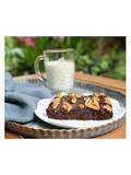 Chocolate brownie with nuts on a white plate with a glass of milk in the background.