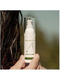 Hand holding a bottle of Dr. Alkaitis Organic Day Creme against a blurred background