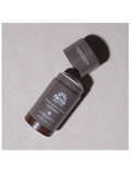 A dark brown deodorant stick from Pacha Soap Co. with its cap off, lying diagonally on a textured light gray background.