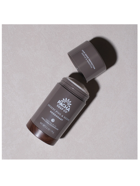 A dark brown deodorant stick from Pacha Soap Co. with its cap off, lying diagonally on a textured light gray background.
