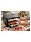Food dehydrator with fruits and vegetables being dried, placed on a kitchen counter.