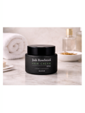 Black jar of Josh Rosebrook hair cream on a marble surface with towels and a bowl in the background.