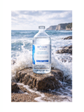 Bottle of Biocean Isotonic water on a rocky beach with ocean waves.