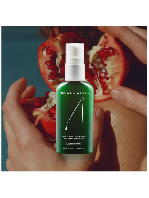 Restoring Eye & Face Makeup Remover, 2oz, by Dr Alkaitis held by a hand with a pomegranate in the background