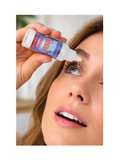 A close-up of a woman applying eye drops from a small white bottle labeled 'Rhin's Tear Water' to her right eye, with her hand holding the bottle.