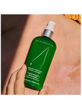 Green bottle of Dr. Alkaitis facial cleanser held against skin
