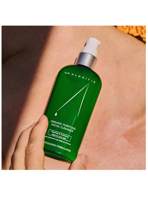 Green bottle of Dr. Alkaitis facial cleanser held against skin