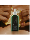 Organic Purifying Facial Cleanser, by Dr Alkaitis on a brown surface with hands holding lemons.