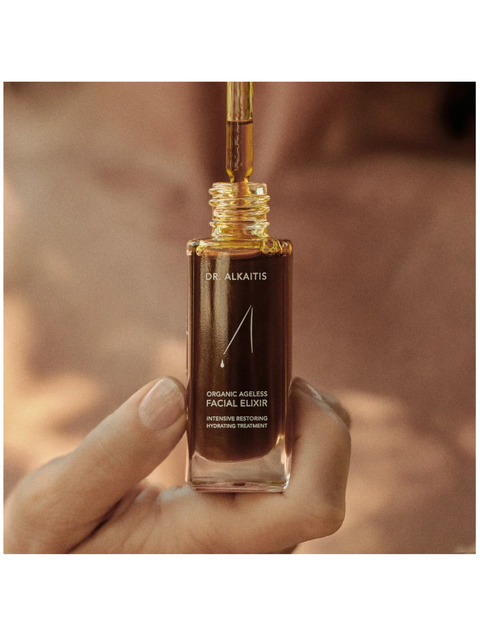Hand holding a bottle of Dr. Alkaitis Organic Nourishing Facial Elixir with a blurred background.