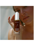 Person holding a bottle of Dr. Alkaitis facial elixir close to their face.