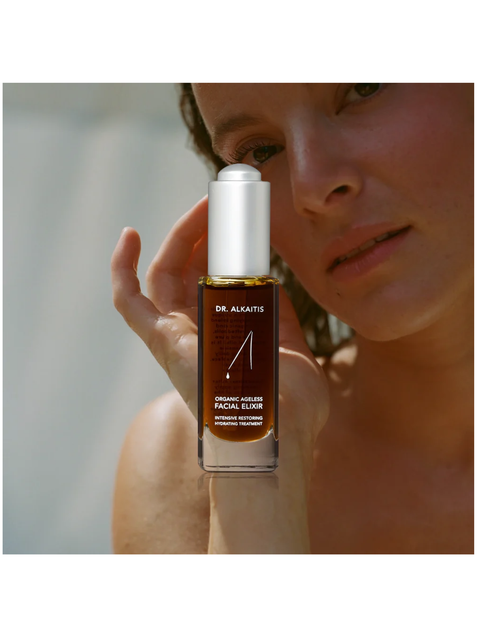 Person holding a bottle of Dr. Alkaitis facial elixir close to their face.