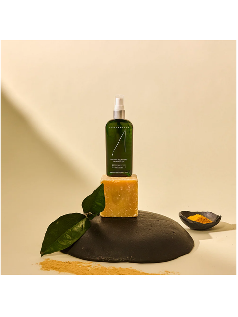 Organic Nourishing Treatment Oil, by Dr Alkaitis, on a yellow bar of soap, and leaves on a beige background