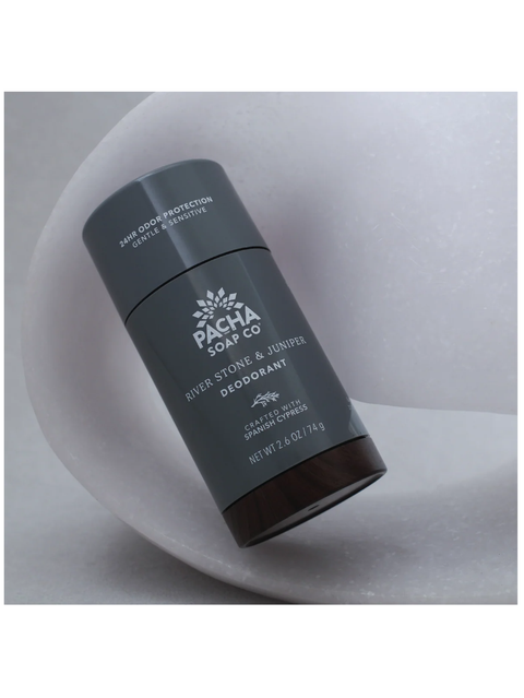 Pacha Soap Co. River Stone & Minerals Deodorant stick in a dark gray cylindrical container with a dark brown base, resting on a white curved surface.