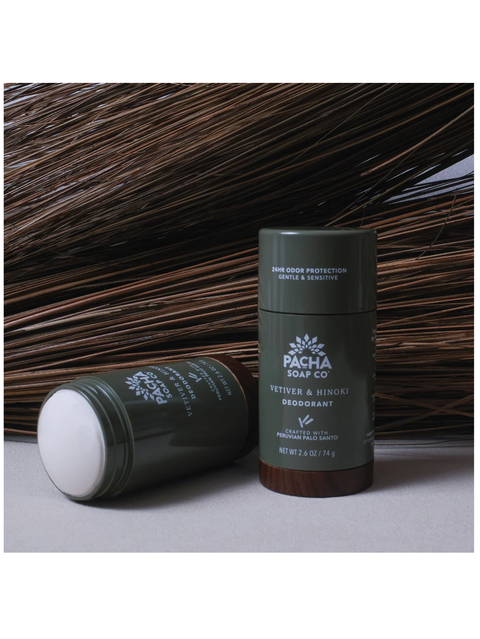 Pacha Soap Co. Vetiver & Hinoki Deodorant shown in two dark olive green tubes, one standing upright and one lying on its side, set against a background of dark brown dried plant fibers.